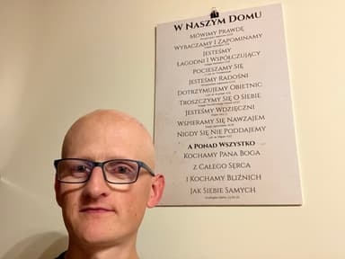 Tablica „W naszym domu” z zasadami życia rodziny i odnośnikami do Pisma, obok mężczyzna