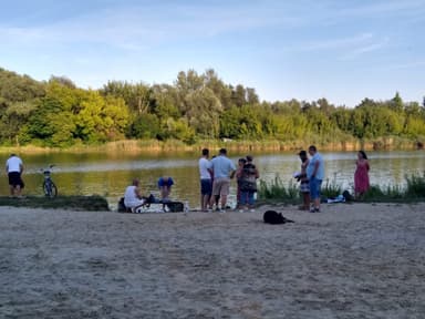 Grupa ludzi na piaszczystym brzegu jeziora podczas chrztu