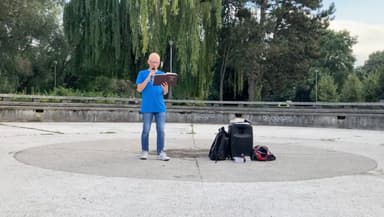 Mężczyzna czyta Pismo Święte do mikrofonu na betonowej estradzie w parku